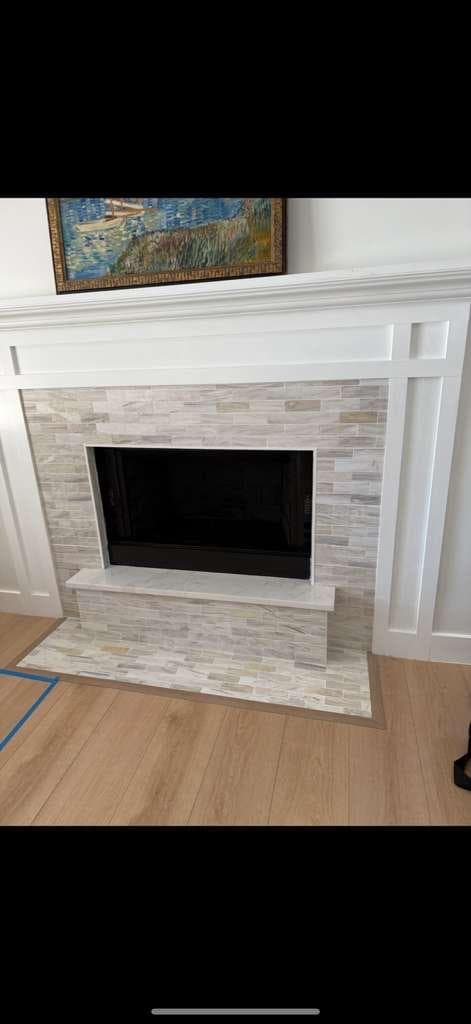 Fireplace with a white mantel and a light-colored tiled surround and raised hearth.